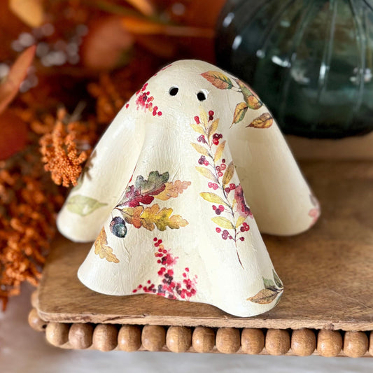 Decorative ghost figurine with floral patterns on a wooden board with autumn-themed decor.