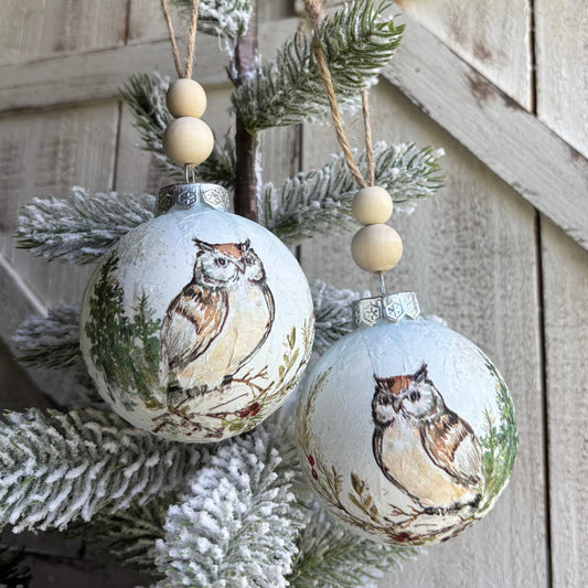 Decorative Christmas ornaments with owl designs on a frosted branch against a wooden background