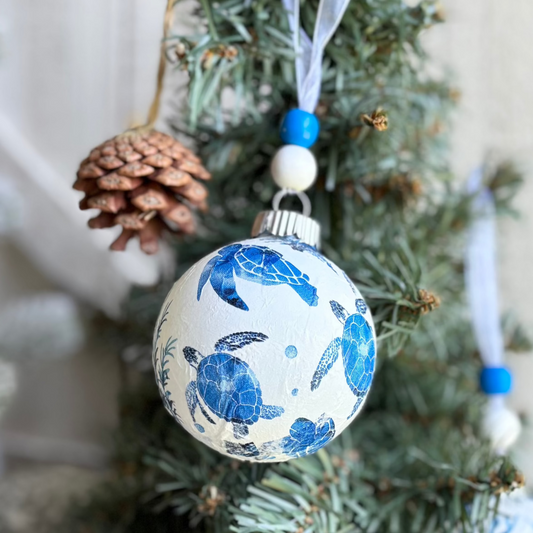 Decorative Christmas ornament with blue turtle design hanging on a tree.