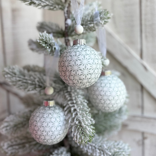 Decorative Christmas tree with frosted branches and silver ornaments against a wooden wall.