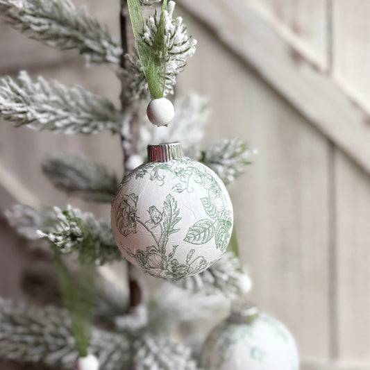 Decorative Christmas ball ornament with floral pattern hanging on a tree.