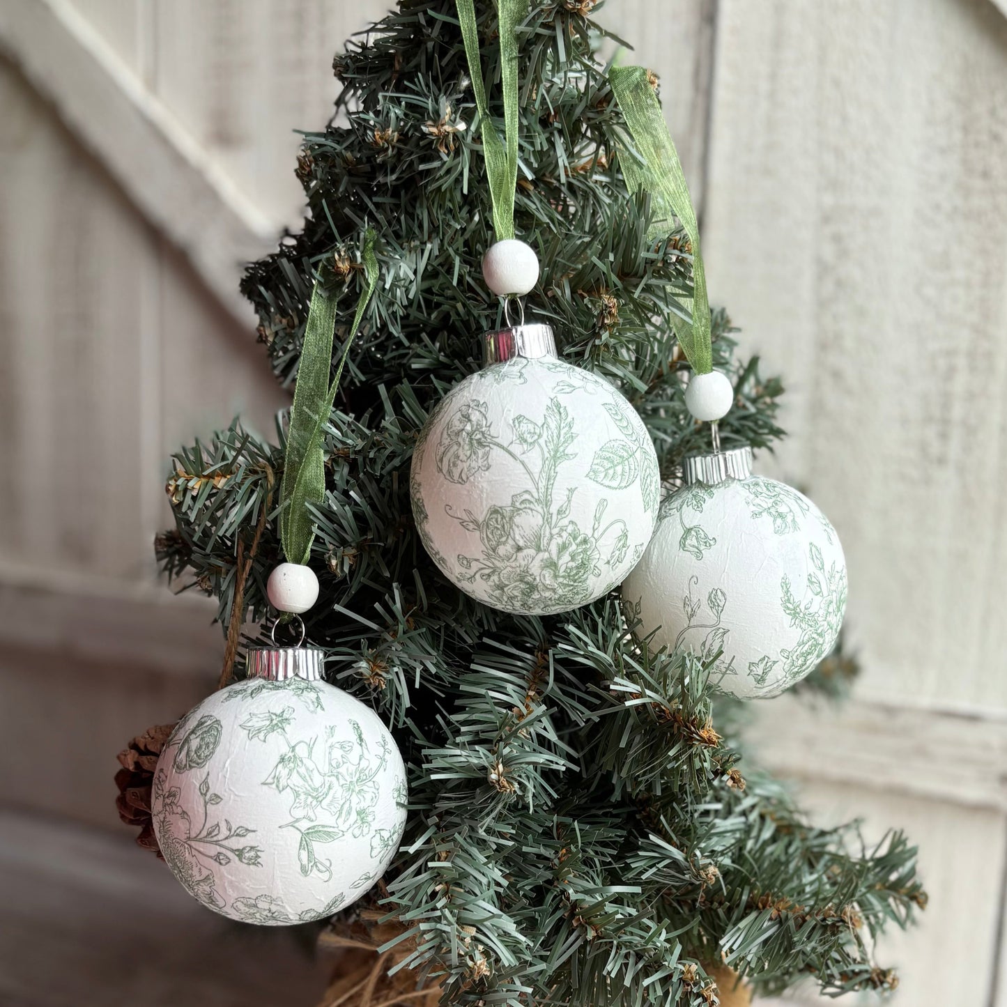 Small decorated Christmas tree with white patterned ornaments on a wooden floor.