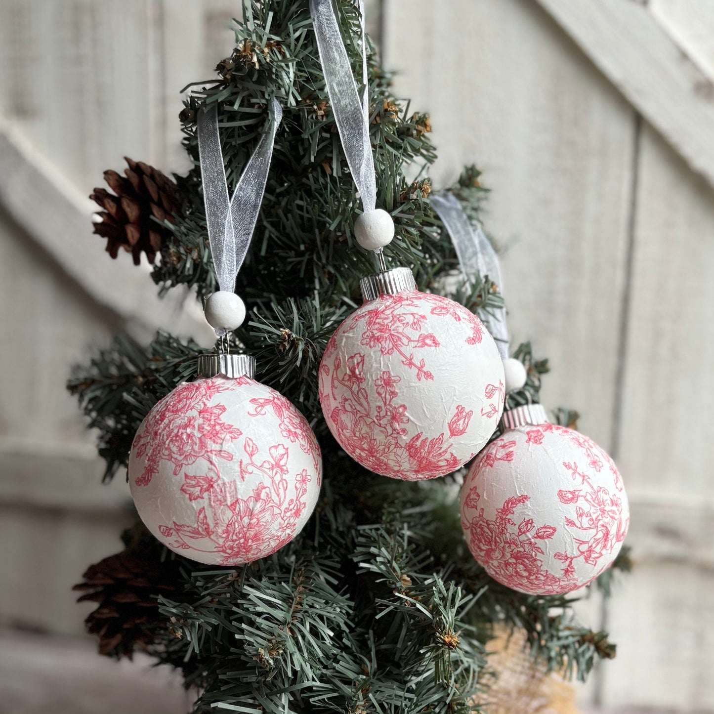 Decorative Christmas ornaments with pink floral patterns hanging on a tree.