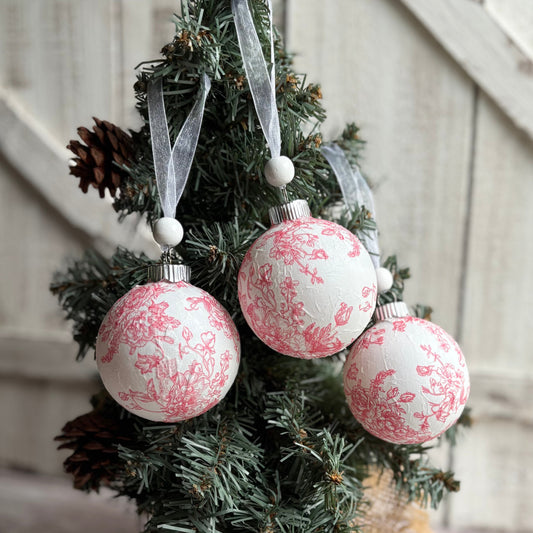 Decorative Christmas ornaments with pink floral patterns hanging on a tree.