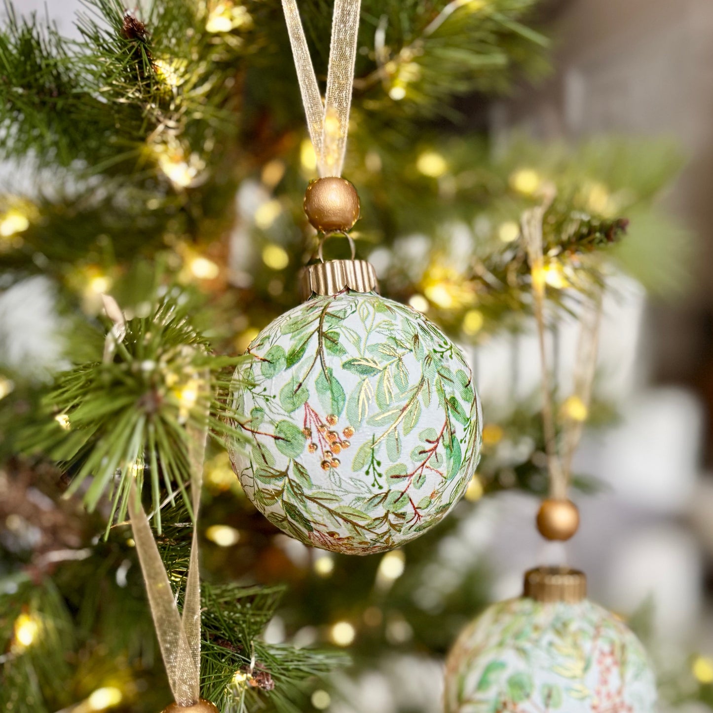 Decorative Christmas ornaments with floral patterns hanging on a tree.