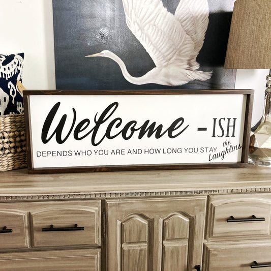 Decorative sign on a wooden dresser with a lamp and basket in the background