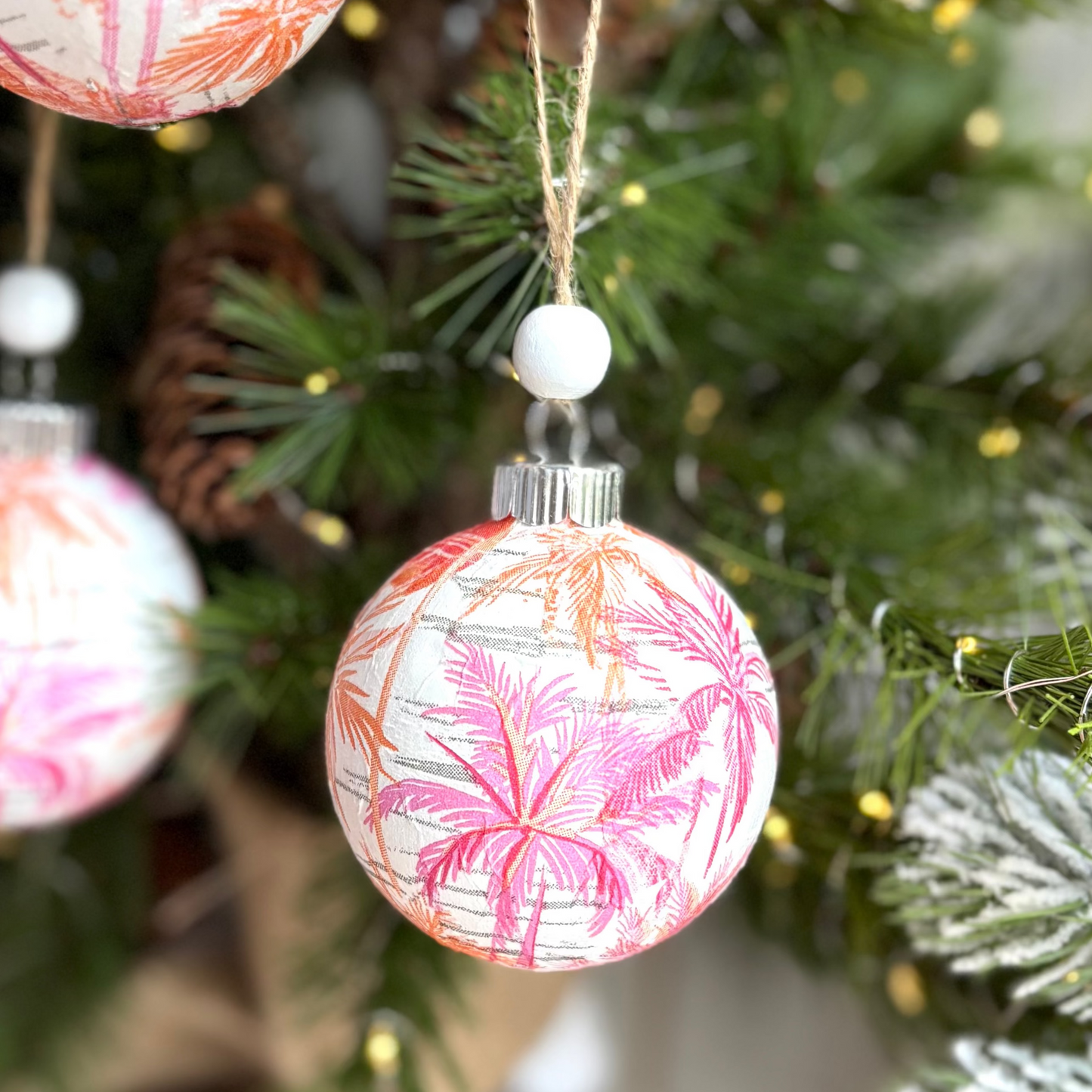 Decorative Christmas ornaments with pink and white floral patterns hanging on a tree.
