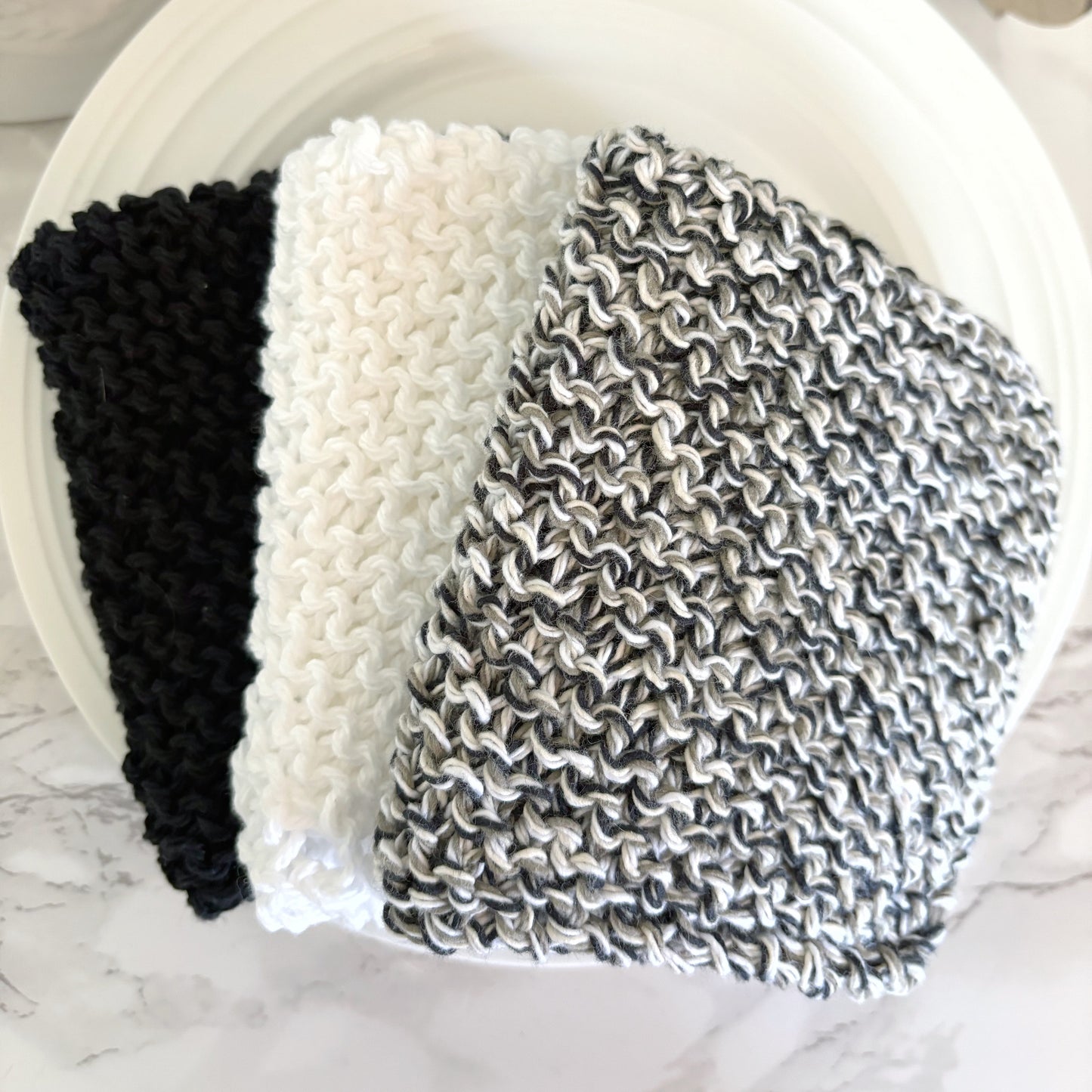 Three knitted headbands in black, white, and patterned gray on a white plate.
