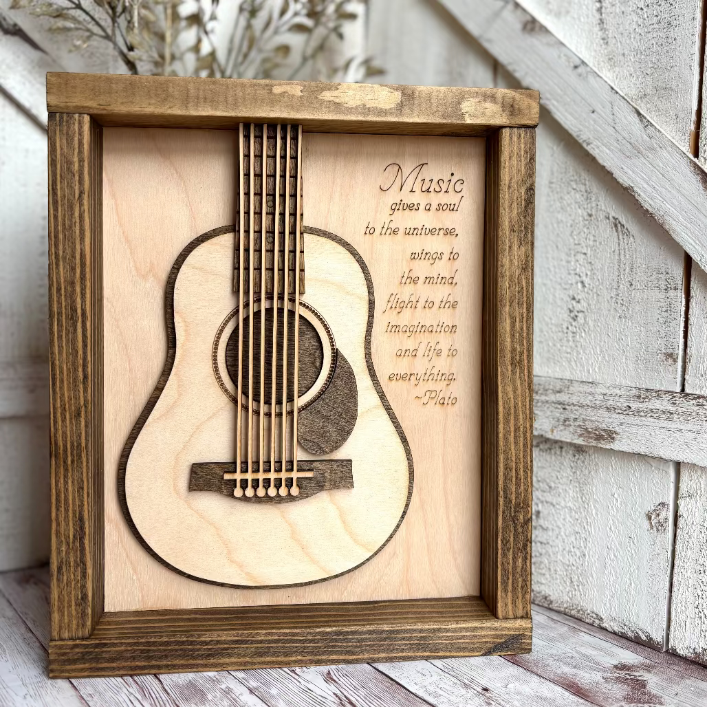 Wooden framed guitar cutout with engraved text on a wooden surface.