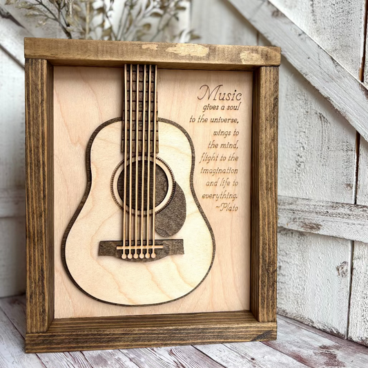 Wooden framed guitar cutout with engraved text on a wooden surface.