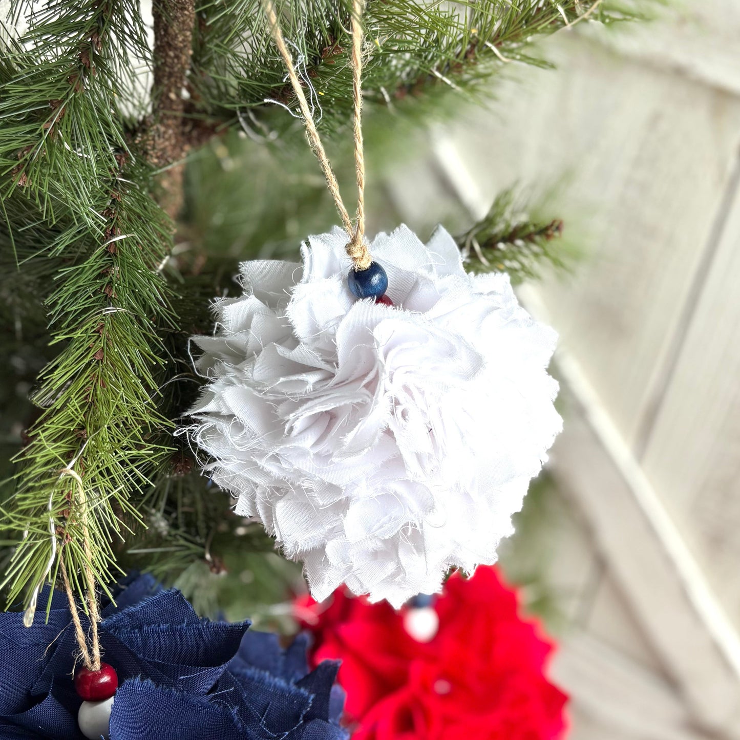Decorative ornaments in red, white, and blue hanging on a Christmas tree.