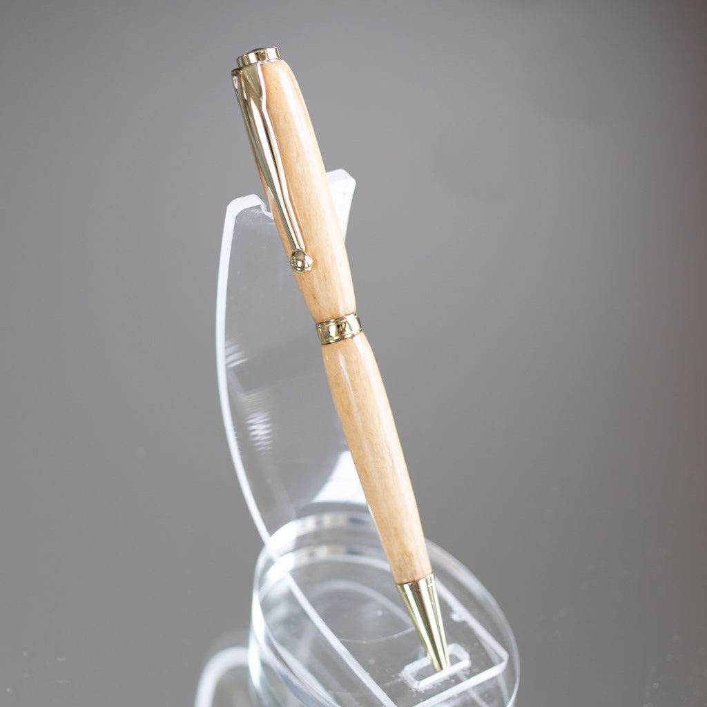 Beige pen with gold accents on a clear stand against a gray background