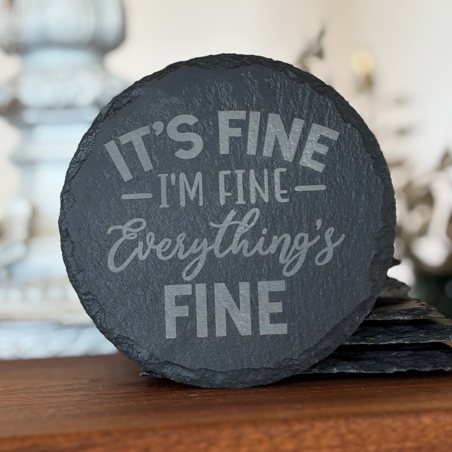 Set of slate coasters with humorous text on a wooden surface