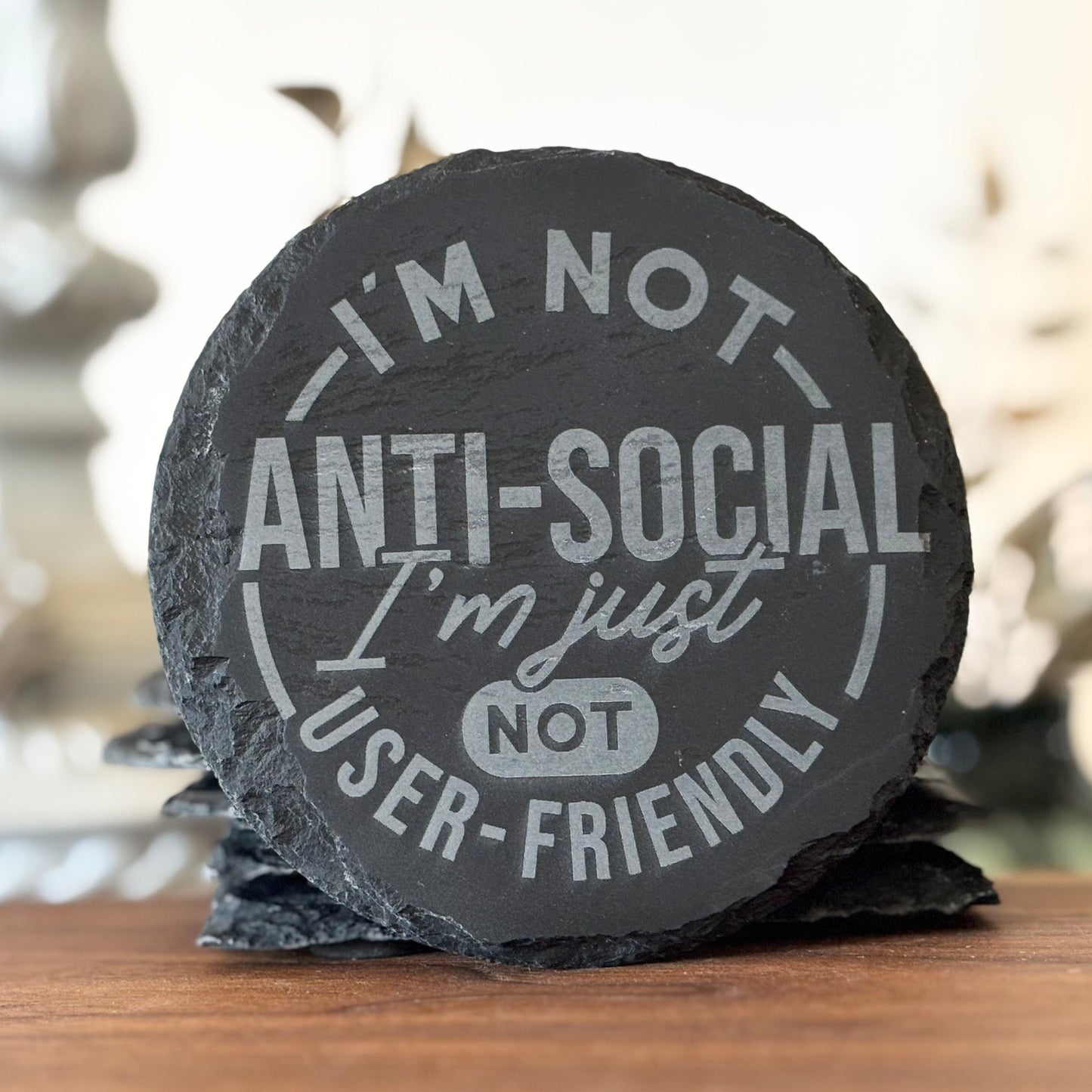 Round slate coaster with humorous text on a wooden surface