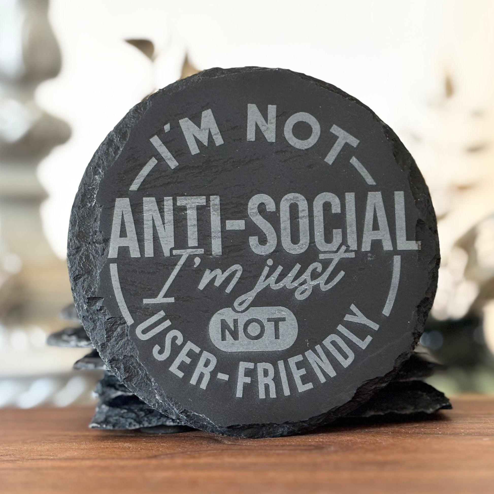 Round slate coaster with humorous text on a wooden surface