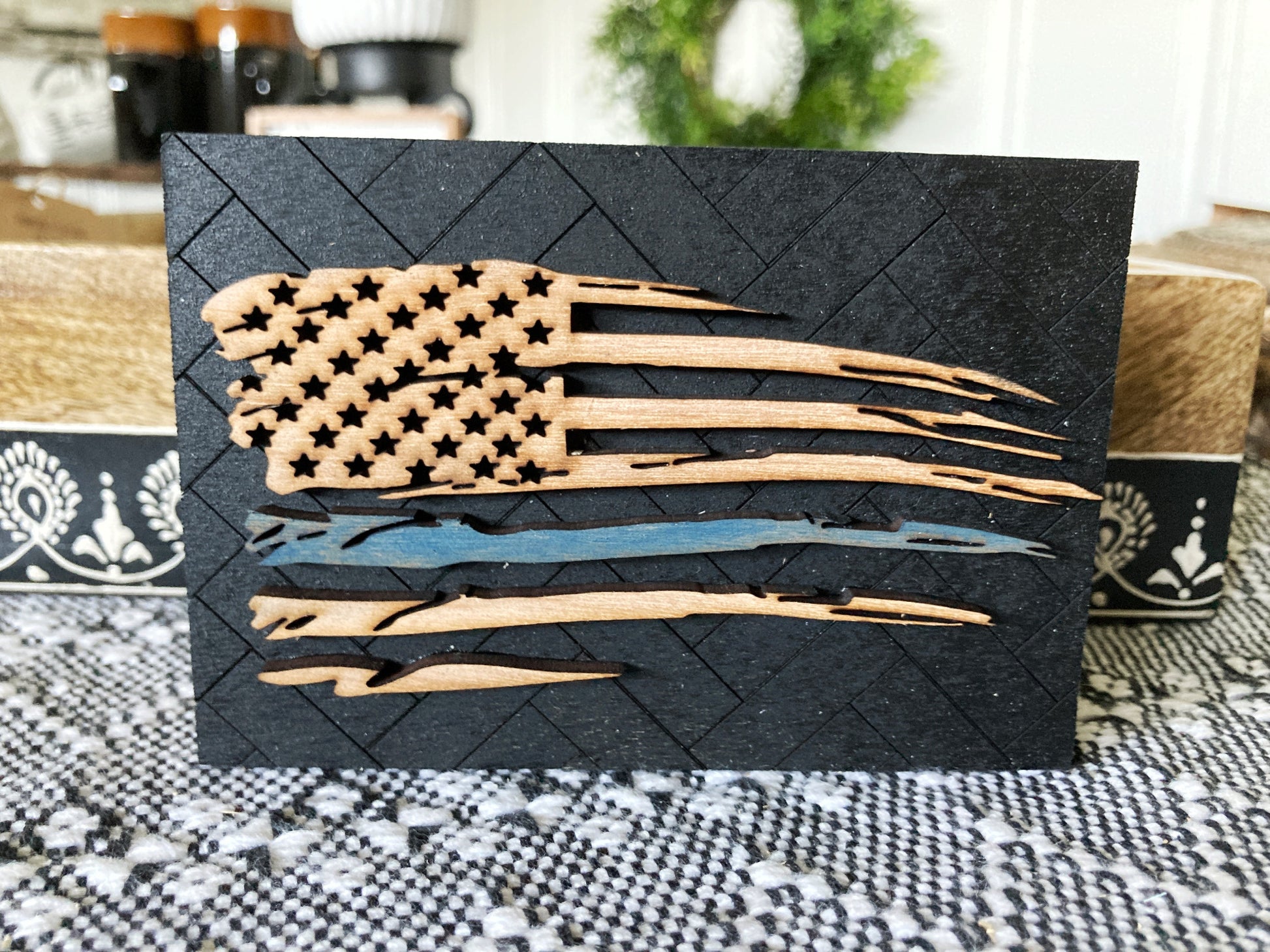 Small sign with an engraved herringbone pattern in the painted black wood background.  The natural wood tattered flag had a thin blue line to support the police is attached to the background