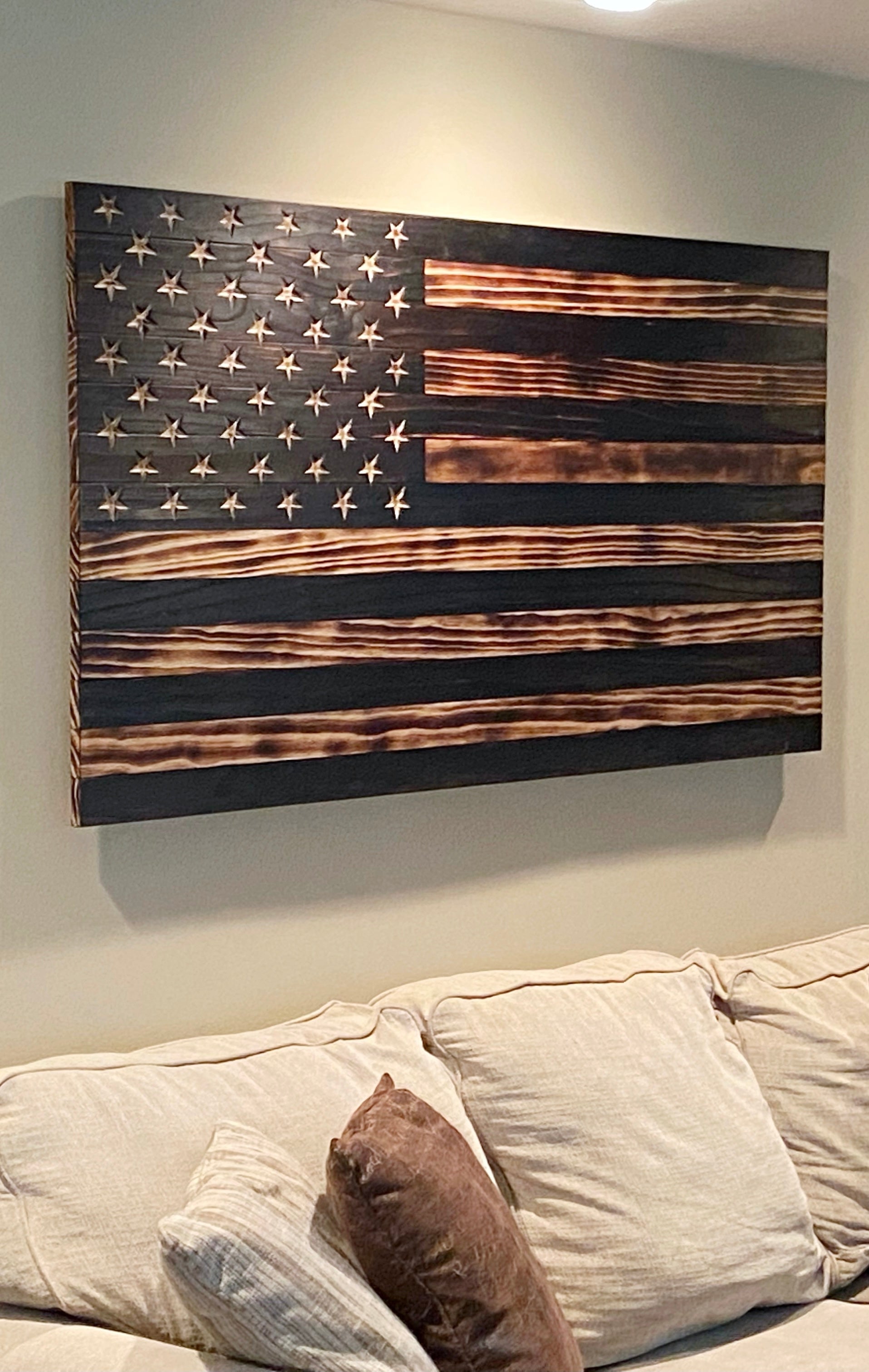 Five foot wooden American flag shown on living room wall. Natural wood  burned to bring out the grain with carved stars in the union