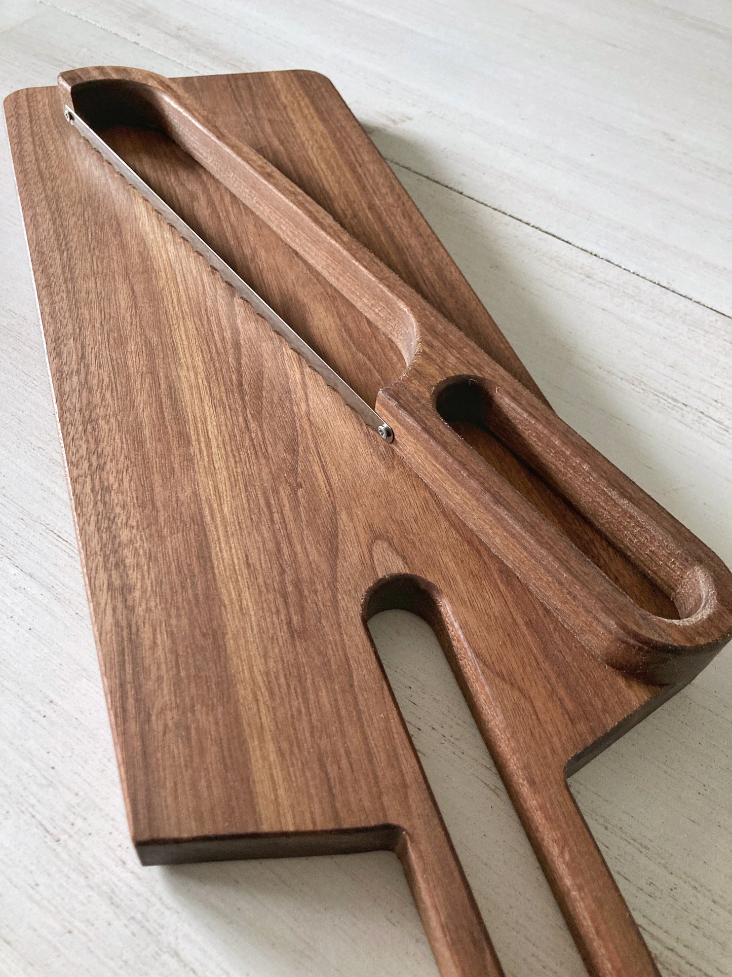 Solid walnut 2 foot long cutting board with a long oval shaped cutout handle. The matching bow cutting knife makes cutiing bread easy and the set beautiful when not in use. Use as a bread board or charcuterie board