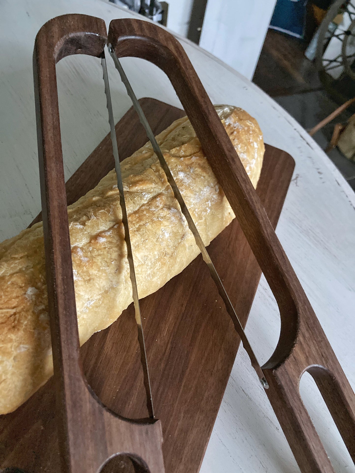 Solid walnut 2 foot long cutting board with a long oval shaped cutout handle. The matching bow cutting knife (in a left or right handed option) makes cutiing bread easy and the set beautiful when not in use. Use as a bread board or charcuterie board